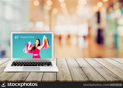 shopping online with labtop, notebook on table top and bokeh background, computer with beautiful asian woman holding shopping bag and smile present on display.