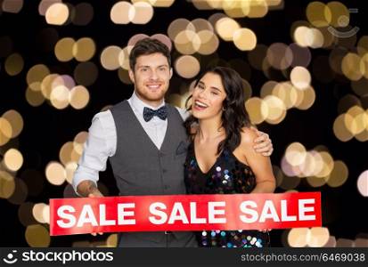 shopping, people and black friday concept - happy couple with red sale sign over night lights background. happy couple with red sale sign