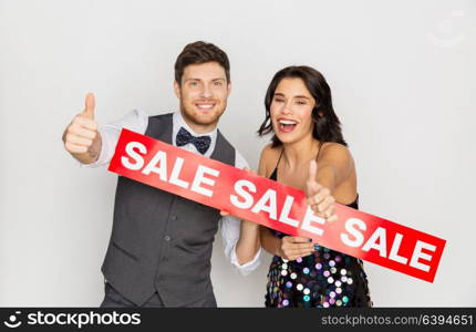 shopping, people and fashion concept - happy couple with red sale sign showing thumbs up. happy couple with red sale sign showing thumbs up