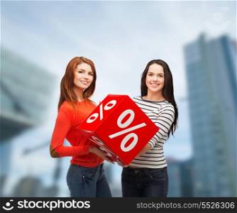 shopping, sale and gift sconcept - two smiling teenage girls with percent sign on red box outdoors