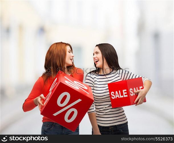 shopping, sale and gift sconcept - two smiling teenage girls with percent and sale sign on red box at street