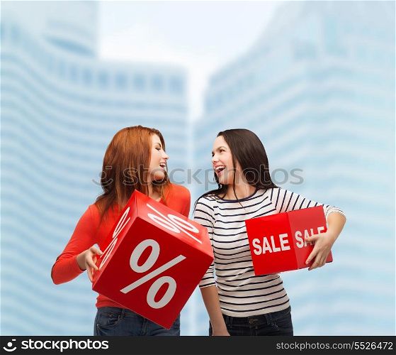 shopping, sale and gift sconcept - two smiling teenage girls with percent and sale sign on red box outdoors