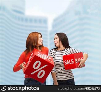 shopping, sale and gift sconcept - two smiling teenage girls with percent and sale sign on red box outdoors