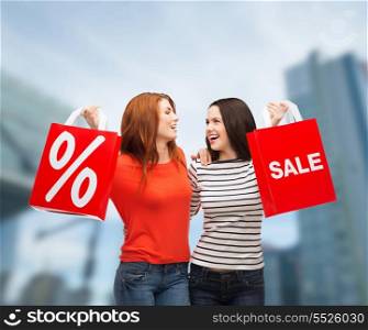 shopping, sale and gift sconcept - two smiling teenage girls with shopping bags and percent sign outdoors