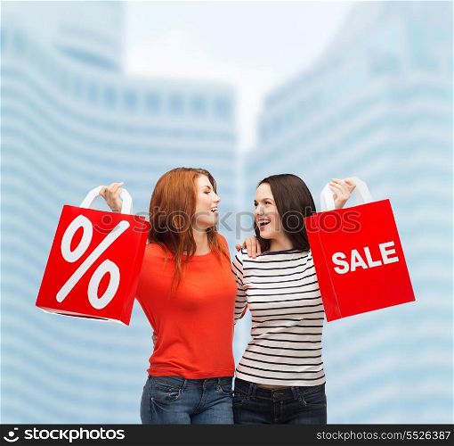 shopping, sale and gift sconcept - two smiling teenage girls with shopping bags and percent sign outdoors
