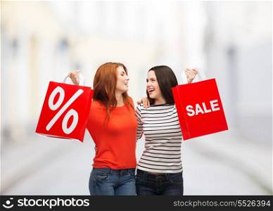 shopping, sale and gift sconcept - two smiling teenage girls with shopping bags and percent sign at street