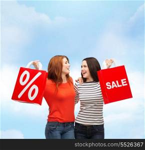 shopping, sale and gift sconcept - two smiling teenage girls with shopping bags and percent sign