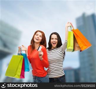 shopping, sale and gifts concept - two smiling teenage girls with shopping bags and credit card