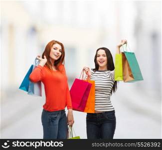 shopping, sale and gifts concept - two smiling teenage girls with shopping bags at street