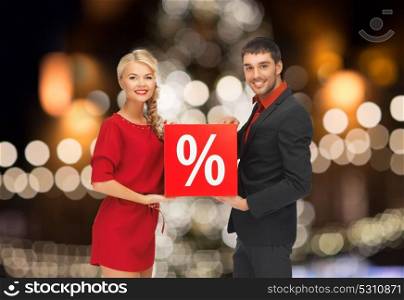 shopping, sale and people concept - happy couple with discount sign over christmas tree lights background. couple with discount sign over christmas lights