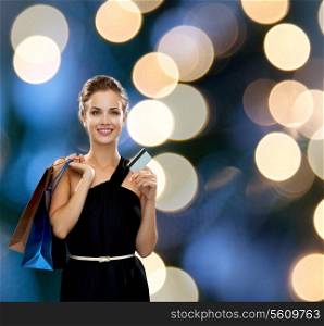 shopping, sale, banking, money and holidays concept - smiling woman in dress with shopping bags and credit card over black background