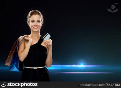 shopping, sale, banking, money and holidays concept - smiling woman in dress with shopping bags and credit card over black background