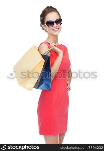 shopping, sale, christmas and holiday concept - smiling elegant woman in red dress and sunglasses with shopping bags