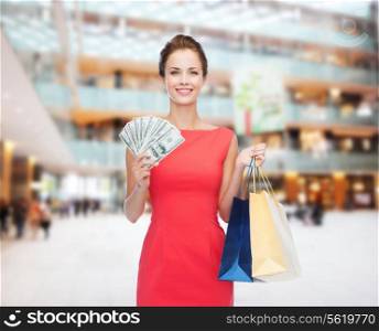 shopping, sale, christmas and holiday concept - smiling elegant woman in red dress with shopping bags and dollars