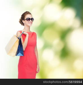 shopping, sale, christmas and holiday concept - smiling elegant woman in red dress and sunglasses with shopping bags