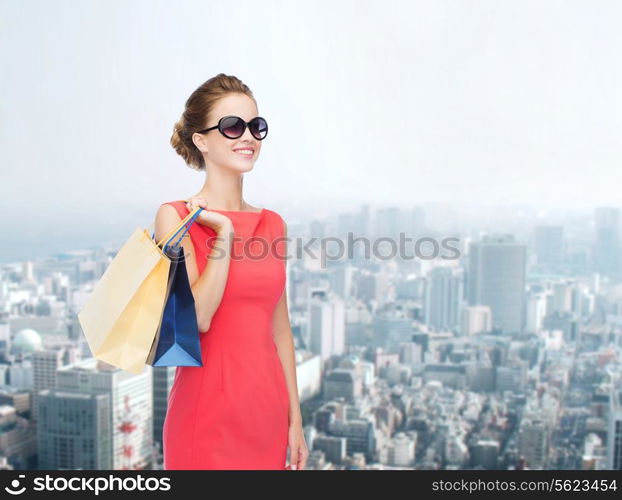 shopping, sale, christmas and holiday concept - smiling elegant woman in red dress and sunglasses with shopping bags