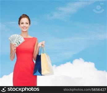 shopping, sale, christmas and holiday concept - smiling elegant woman in red dress with shopping bags and dollars