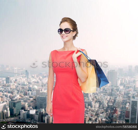 shopping, sale, christmas and holiday concept - smiling elegant woman in red dress and sunglasses with shopping bags