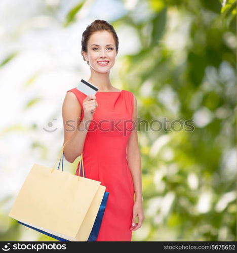 shopping, sale, christmas and holiday concept - smiling elegant woman in red dress with shopping bags and plastic card