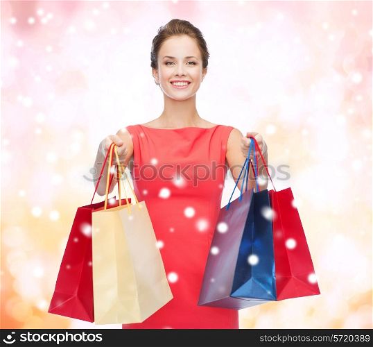 shopping, sale, christmas and holiday concept - smiling elegant woman in red dress with shopping bags over pink snowy background