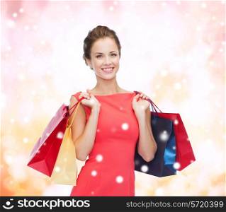 shopping, sale, christmas and holiday concept - smiling elegant woman in red dress with shopping bags over pink snowy background