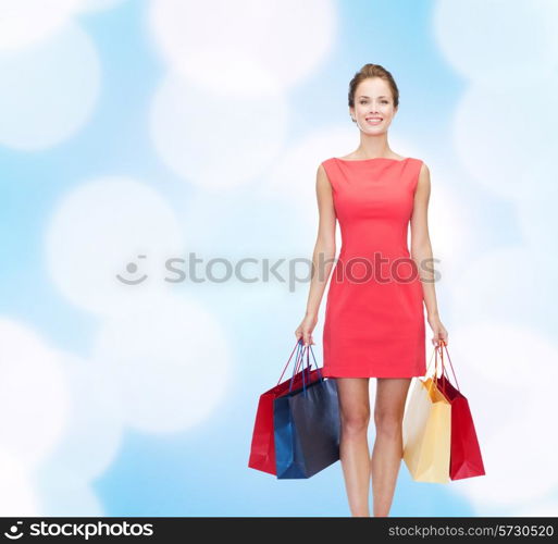 shopping, sale, christmas and holidays concept - smiling elegant woman in red dress with shopping bags over blue lights background