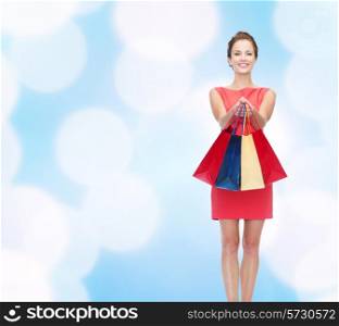 shopping, sale, christmas and holidays concept - smiling elegant woman in red dress with shopping bags over blue lights background