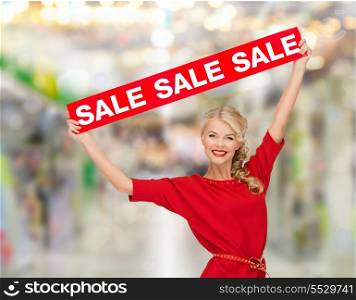 shopping, sale, christmas and mall concept - smiling woman in dress with red sale sign at shopping mall