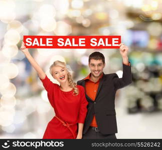 shopping, sale, christmas, couple and mall concept - smiling woman and man with red sale sign at shopping mall