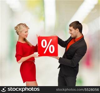 shopping, sale, christmas, couple and mall concept - smiling woman and man with red percent sale sign at shopping mall