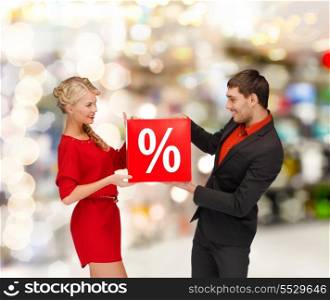 shopping, sale, christmas, couple and mall concept - smiling woman and man with red percent sale sign at shopping mall