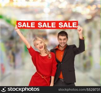 shopping, sale, christmas, couple and mall concept - smiling woman and man with red sale sign at shopping mall