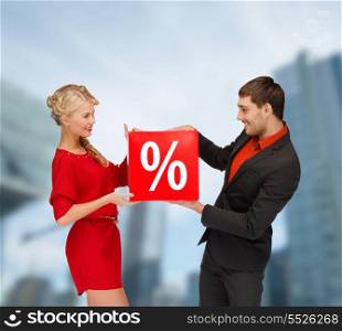 shopping, sale, christmas, couple and x-mas concept - smiling woman and man with red percent sale sign outdoors