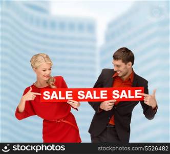 shopping, sale,christmas, couple and x-mas concept - smiling woman and man with red sale sign outdoors