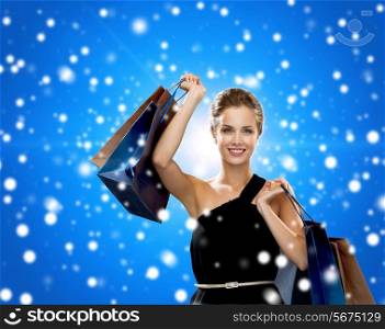 shopping, sale, christmas, people and holidays concept - smiling woman in evening dress with shopping bags over blue snowy background