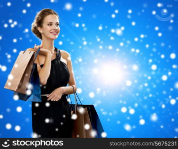 shopping, sale, christmas, people and holidays concept - smiling woman in evening dress with shopping bags over blue snowy background