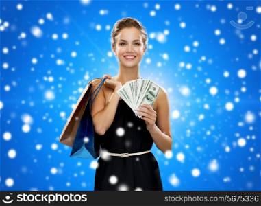 shopping, sale, christmas, people and holidays concept - smiling woman in evening dress with shopping bags over blue snowy background