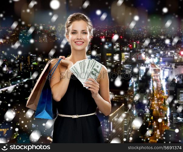 shopping, sale, christmas, people and holidays concept - smiling woman in evening dress with shopping bags over snowy night city background