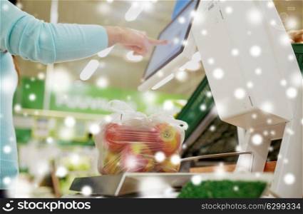 shopping, sale, consumerism and people concept - female customer weighing apples on scale at grocery store over snow. woman weighing apples on scale at grocery store