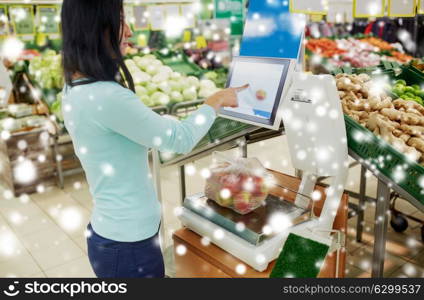 shopping, sale, consumerism and people concept - female customer weighing apples on scale at grocery store over snow. customer weighing apples on scale at grocery store