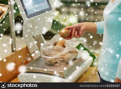 shopping, sale, consumerism and people concept - female customer weighing potatoes on scale at grocery store over snow. customer with potatoes on scale at grocery store
