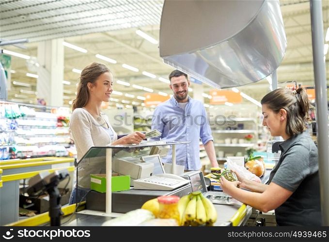 shopping, sale, consumerism and people concept - happy couple buying food at grocery store or supermarket cash register and paying cash money to cashier . couple buying food at grocery store cash register
