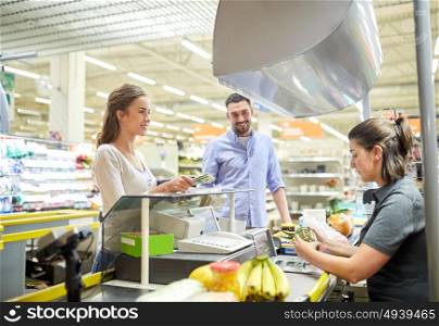 shopping, sale, consumerism and people concept - happy couple buying food at grocery store or supermarket cash register and paying cash money to cashier . couple buying food at grocery store cash register