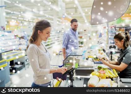 shopping, sale, consumerism and people concept - happy couple buying food at grocery store or supermarket cash register and swiping customer card over snow. couple buying food at grocery store cash register