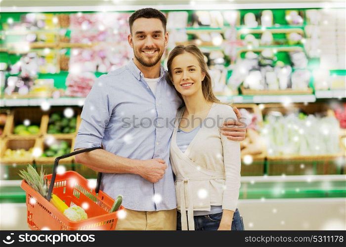 shopping, sale, consumerism and people concept - happy couple with food basket at grocery store or supermarket over snow. happy couple with food basket at grocery store