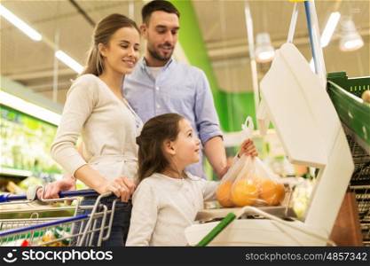shopping, sale, consumerism and people concept - happy family with child weighing oranges on scale at grocery store