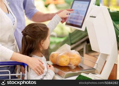 shopping, sale, consumerism and people concept - happy family with child weighing oranges on scale at grocery store. family weighing oranges on scale at grocery store. family weighing oranges on scale at grocery store