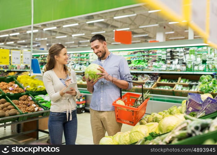shopping, sale, consumerism and people concept - happy young couple with food basket and notebook at grocery store or supermarket