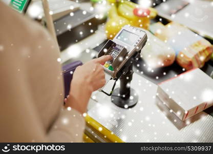 shopping, sale, consumerism and people concept - woman buying food at grocery store or supermarket cash register and entering pin code over snow. woman entering pin code at store cash register