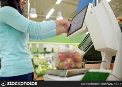 shopping, sale, consumerism and people concept - woman weighing apples on scale at grocery store